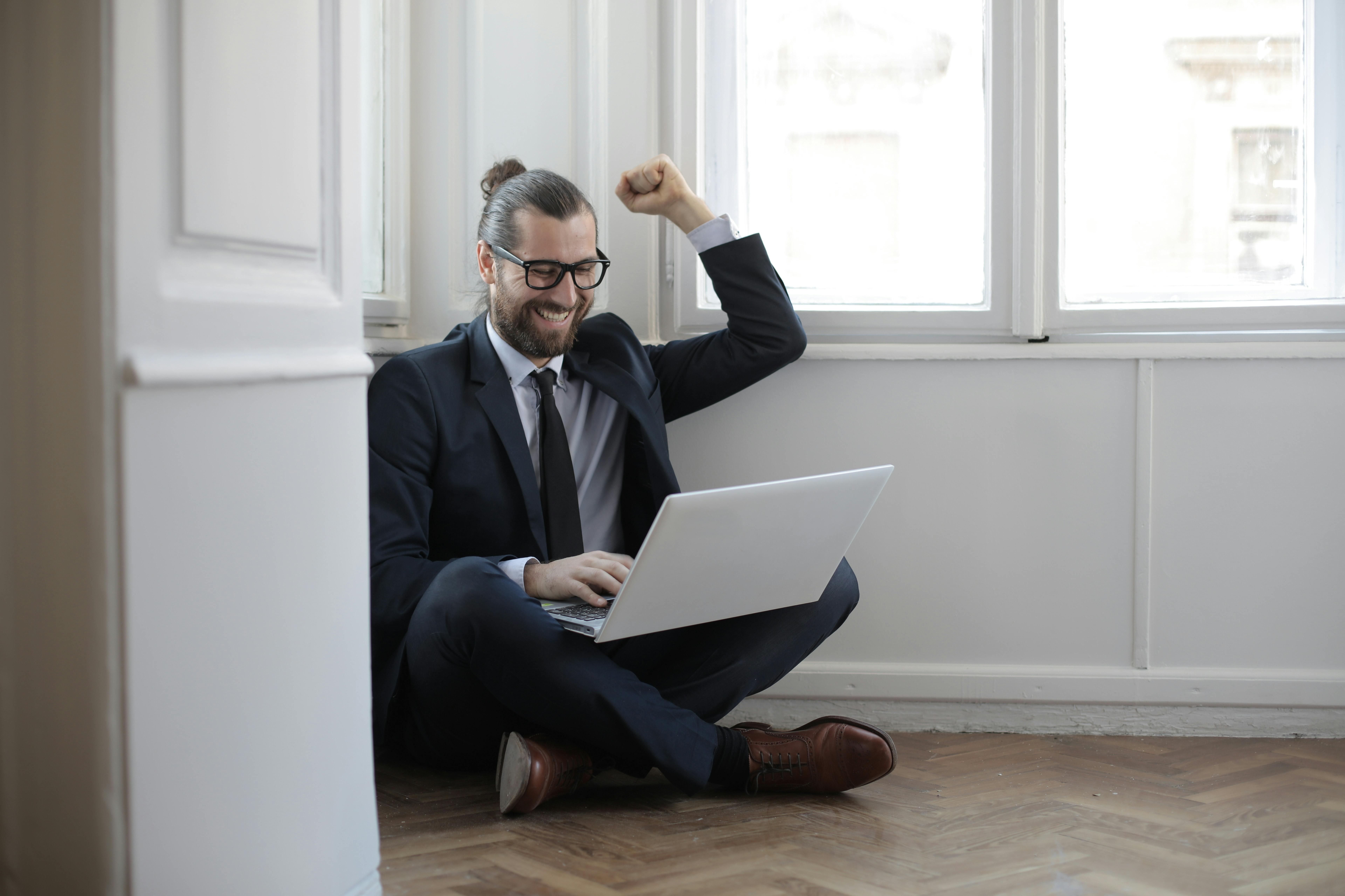A man celebrates with a fist pump his laptop open in lap