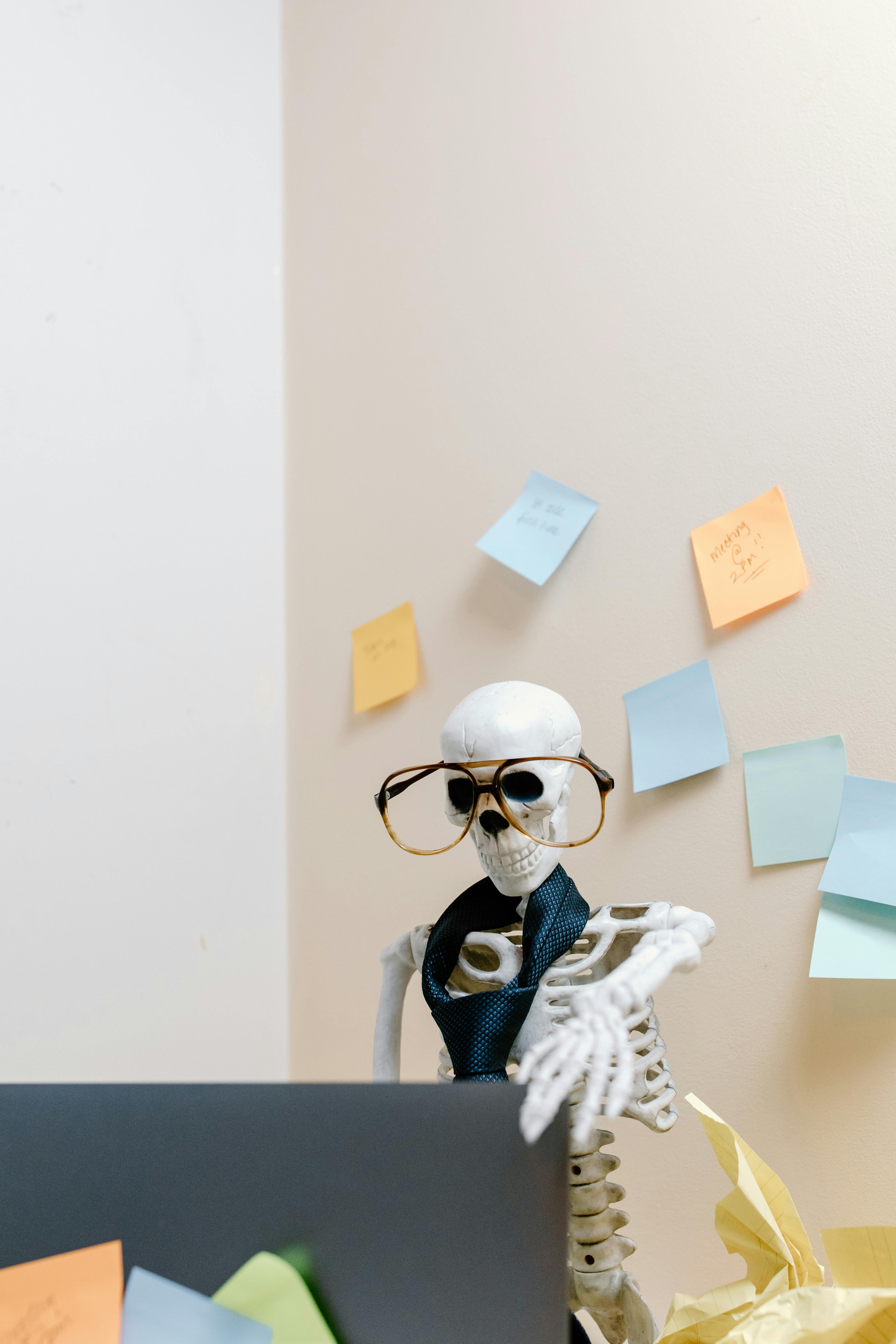 A skeleton sits at a computer wearing a tie